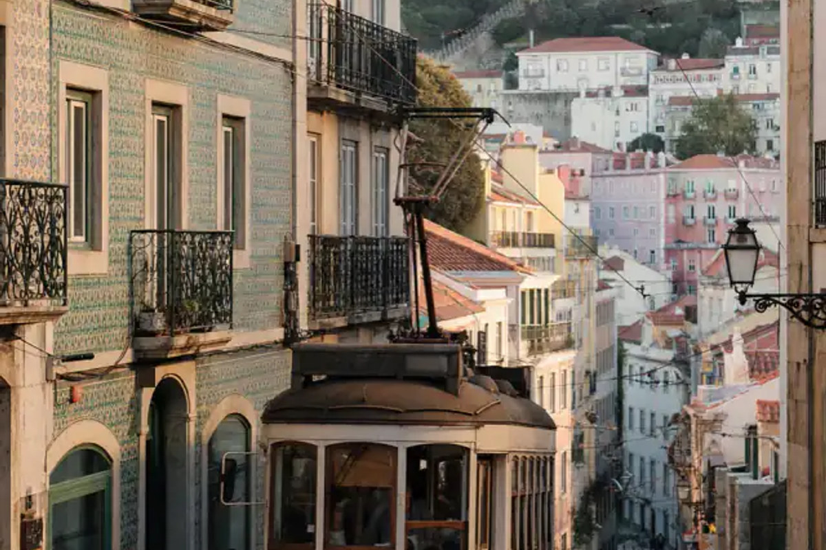 Lisbon hillside street with a yellow tram, tiled facades, and overhead cables