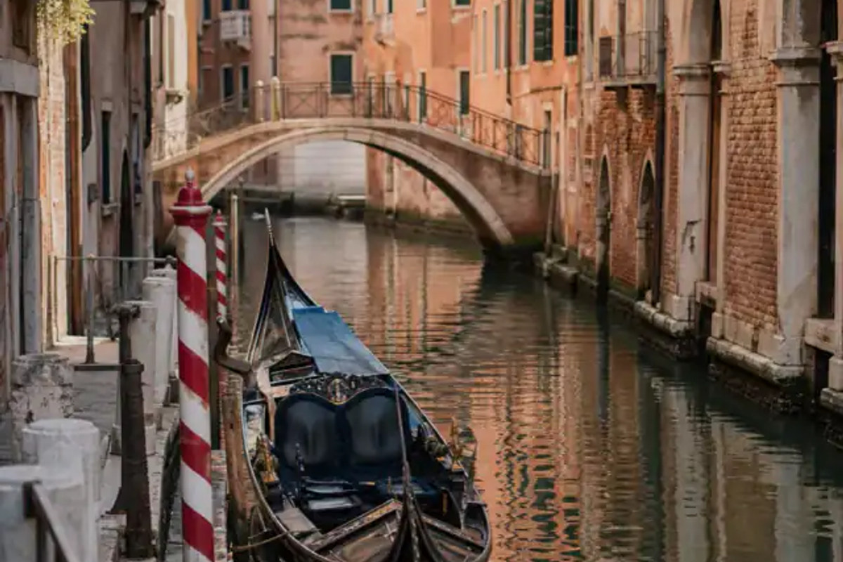 Venice canal with a gondola, striped mooring pole, brick bridge, and aged facades